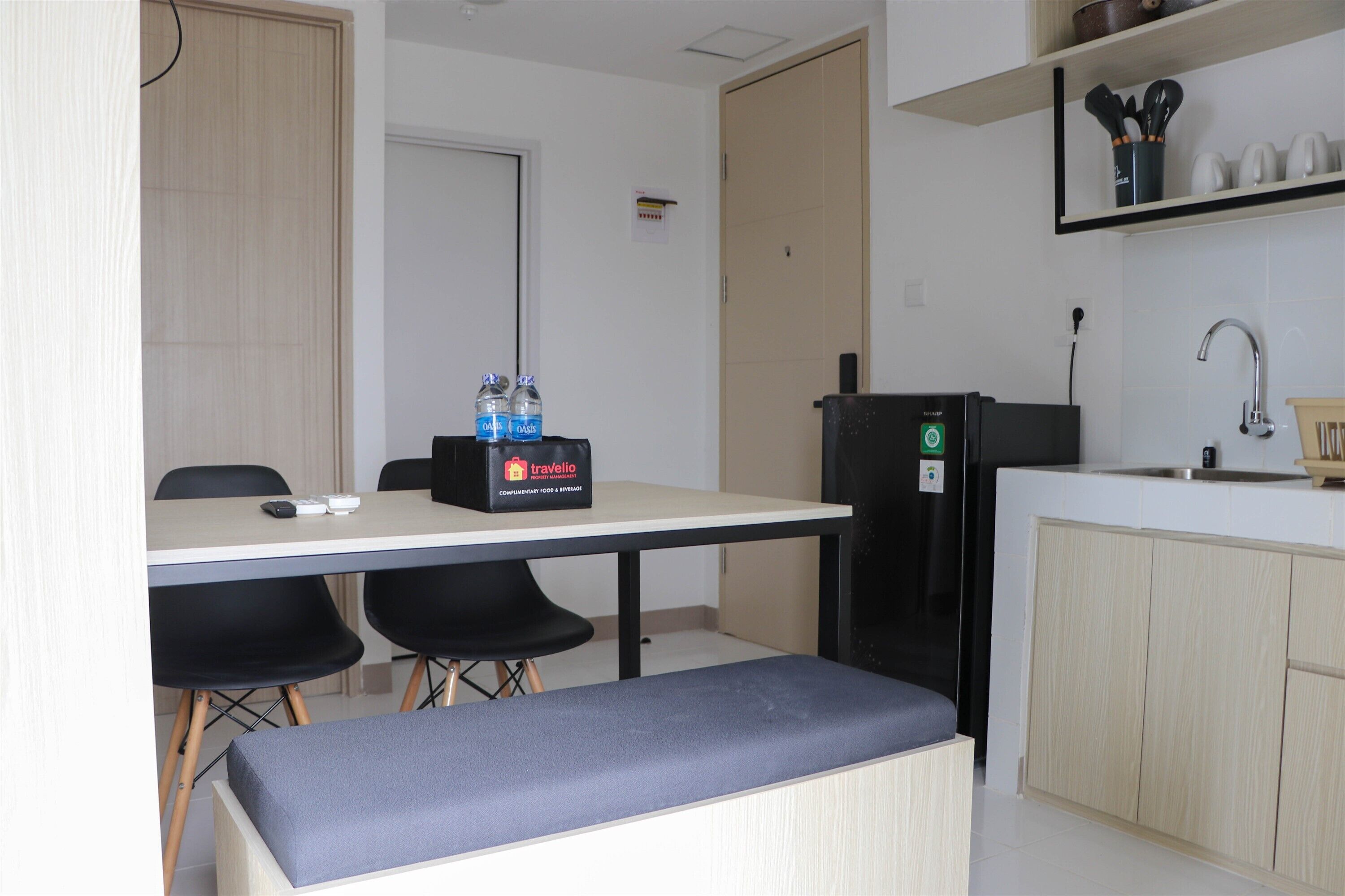 A compact kitchen with a refrigerator, a sink, and a countertop. There are two chairs and a bench at the dining table.