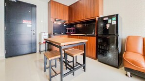 Une cuisine de taille réduite avec des meubles en bois, un réfrigérateur noir, une table en bois avec des tabourets et une porte noire.
