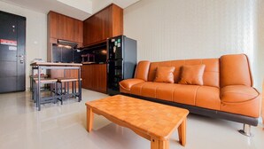 Un salon moderne avec un canapé en cuir, une table basse en bois et un coin cuisine doté de meubles en bois et d’un réfrigérateur.