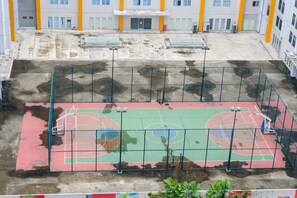 Ein Basketballplatz im Freien mit grüner und roter Oberfläche, umgeben von einem Metallzaun.