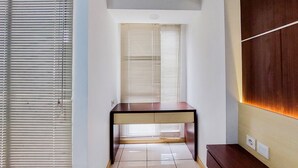 A modern room with a wooden desk, a window with blinds, and a wall-mounted shelf. - Fancy And Nice Studio Apartment At 19Th Floor M-Town Residence Travelio (Gading Serpong)