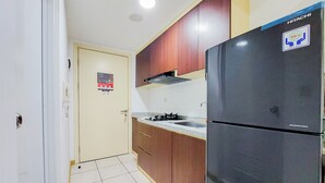 A compact kitchen with a black refrigerator, wooden cabinets, a gas stove, and a tiled floor. - Fancy And Nice Studio Apartment At 19Th Floor M-Town Residence Travelio (Gading Serpong)