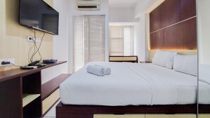 A hotel room with a bed, a TV, a desk, and a window with blinds. - Fancy And Nice Studio Apartment At 19Th Floor M-Town Residence Travelio (Gading Serpong)