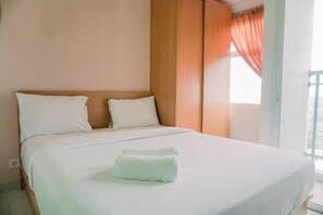 Ein ordentlich bezogenes Bett mit weißen Leinen und zwei Kissen, ein Holz-Kopfteil und ein Fenster mit orangefarbenen Vorhängen.