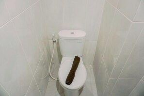 Toilette mit einem braunen Handtuch auf dem Sitz, einem weißen Toilettenpapierhalter und einem sichtbaren Spülhebel.