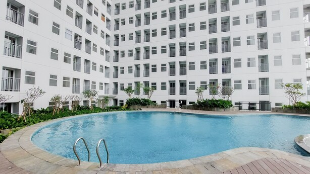 A modern building with a large pool surrounded by a wooden deck. - Nice And Homey Studio Serpong Garden Apartment (Cisauk)