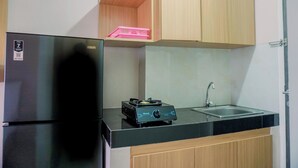 A kitchen with a black refrigerator, a sink, and a small countertop with a portable gas stove. - Nice And Homey Studio Serpong Garden Apartment (Cisauk)
