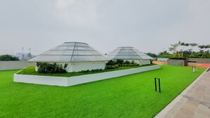 A rooftop garden with two glass greenhouses, surrounded by white planters and green artificial grass. - Nice And Homey Studio Serpong Garden Apartment (Cisauk)