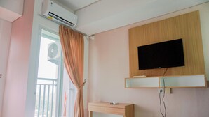 A hotel room with a bed, a TV mounted on the wall, a small wooden desk, and an air conditioning unit. - Nice And Homey Studio Serpong Garden Apartment (Cisauk)