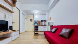 Un espace de vie compact comprenant un canapé rouge, un téléviseur, un coin cuisine et un plancher en bois.