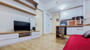 Un appartement moderne avec un téléviseur posé sur un meuble en bois, un canapé rouge, une cuisine avec des placards blancs et un plancher en bois.