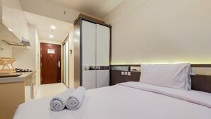 Une chambre d’hôtel avec un lit bien fait, une salle de bain séparée avec un miroir et un petit coin cuisine.
