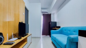 A modern living room with a blue sofa, a television, and a wooden panel wall. - Best Deal And Comfortable 2Br Serpong Garden Apartment (Cisauk)