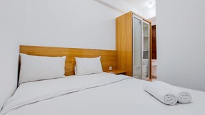 A neatly made bed with white linens and pillows, a wooden headboard, and a wooden wardrobe with a mirror. - Best Deal And Comfortable 2Br Serpong Garden Apartment (Cisauk)