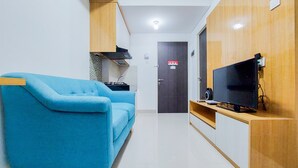 A modern living room with a blue sofa, a flat-screen TV, wooden cabinets, and a kitchen area with a stove and microwave. - Best Deal And Comfortable 2Br Serpong Garden Apartment (Cisauk)