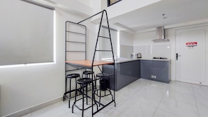 A modern kitchen with a central island, bar stools, a ladder, and a window. - Spacious And Elegant 3Br Loft At Kingland Avenue Apartment (South Tangerang)