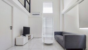 A modern living room with a grey sofa, a white entertainment unit, and a round table. - Spacious And Elegant 3Br Loft At Kingland Avenue Apartment (South Tangerang)