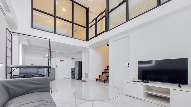 A spacious living area with a large flat-screen TV, a grey sofa, and a glass coffee table. - Spacious And Elegant 3Br Loft At Kingland Avenue Apartment (South Tangerang)