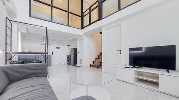 A spacious living area with a large flat-screen TV, a grey sofa, and a glass coffee table.