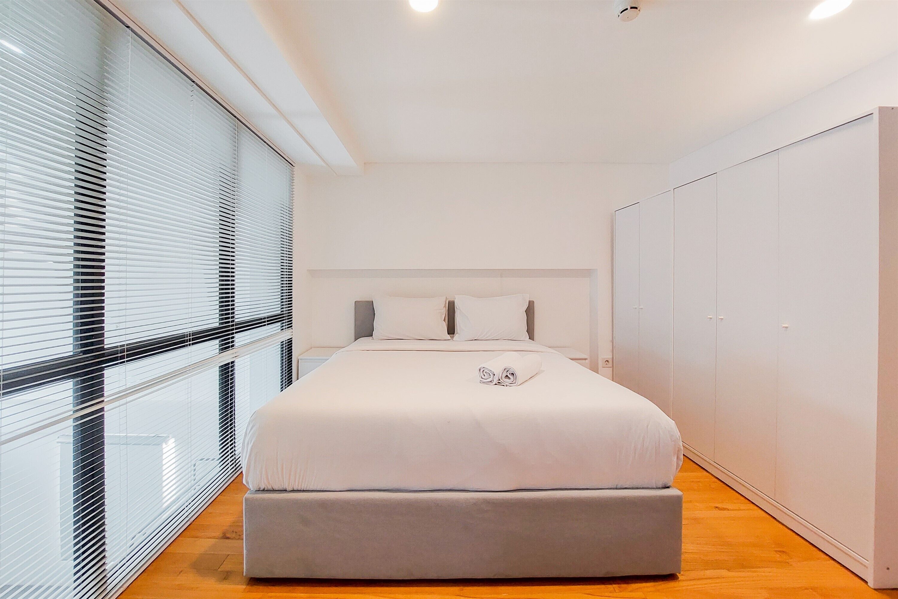 A modern bedroom with a large bed, a grey bench, and a wardrobe.