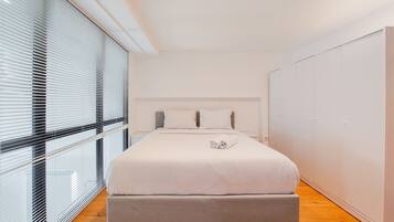 A modern bedroom with a large bed, a grey bench, and a wardrobe.