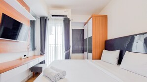 A modern hotel room with a large bed, a flat-screen TV mounted on the wall, a wooden desk, and a window with curtains. - Best Choice And Homey Studio Serpong Garden Apartment (Cisauk)