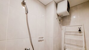 A bathroom with white tiles, a shower with a handheld showerhead, a toilet, and a towel rack. - Best Choice And Homey Studio Serpong Garden Apartment (Cisauk)