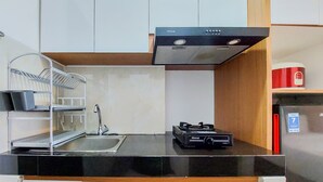 A modern kitchen with white cabinets, a black countertop, a stainless steel range hood, a sink, and a red appliance. - Best Choice And Homey Studio Serpong Garden Apartment (Cisauk)