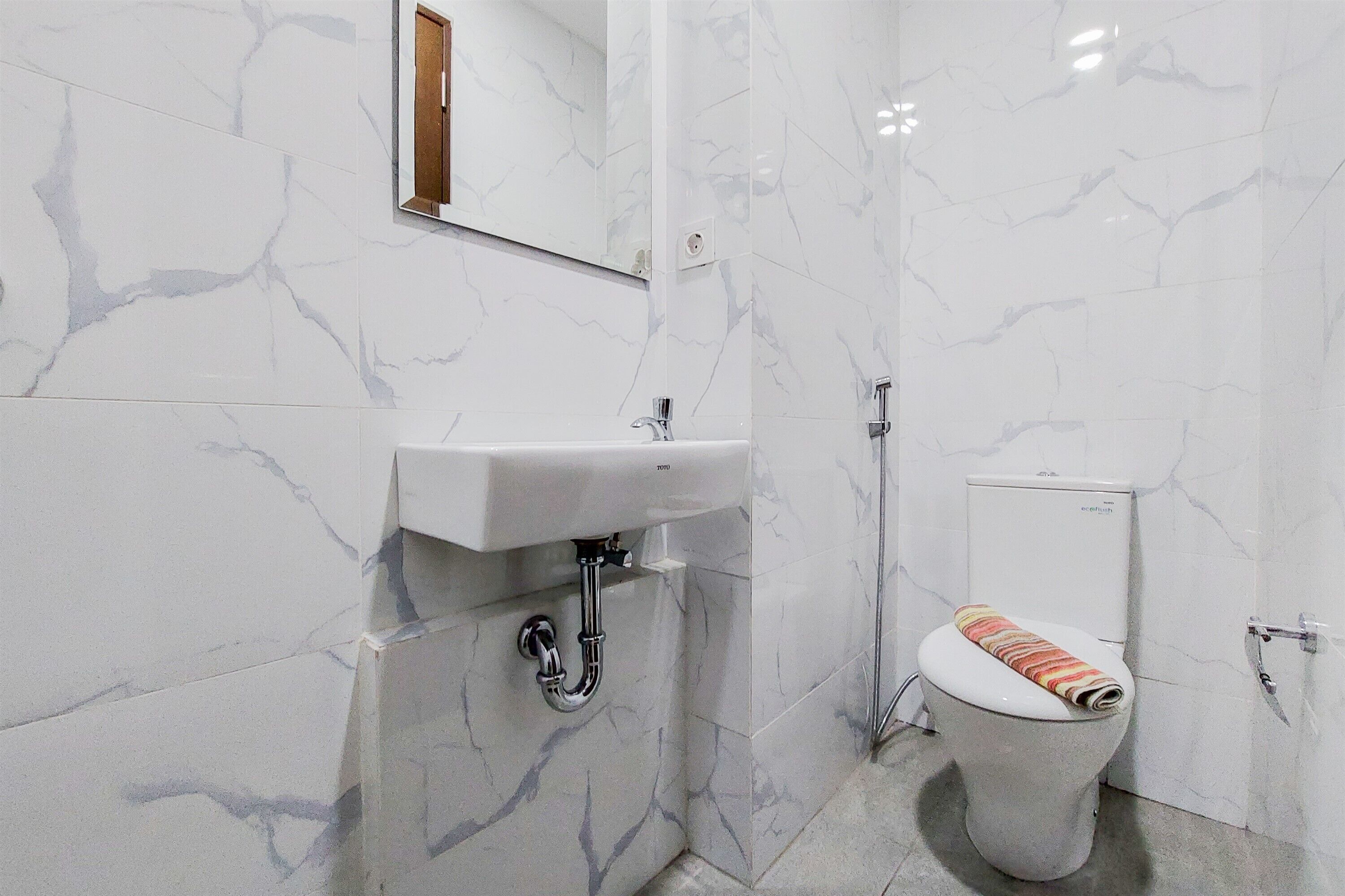 A bathroom with white marble walls, a white sink, and a toilet with a striped towel.