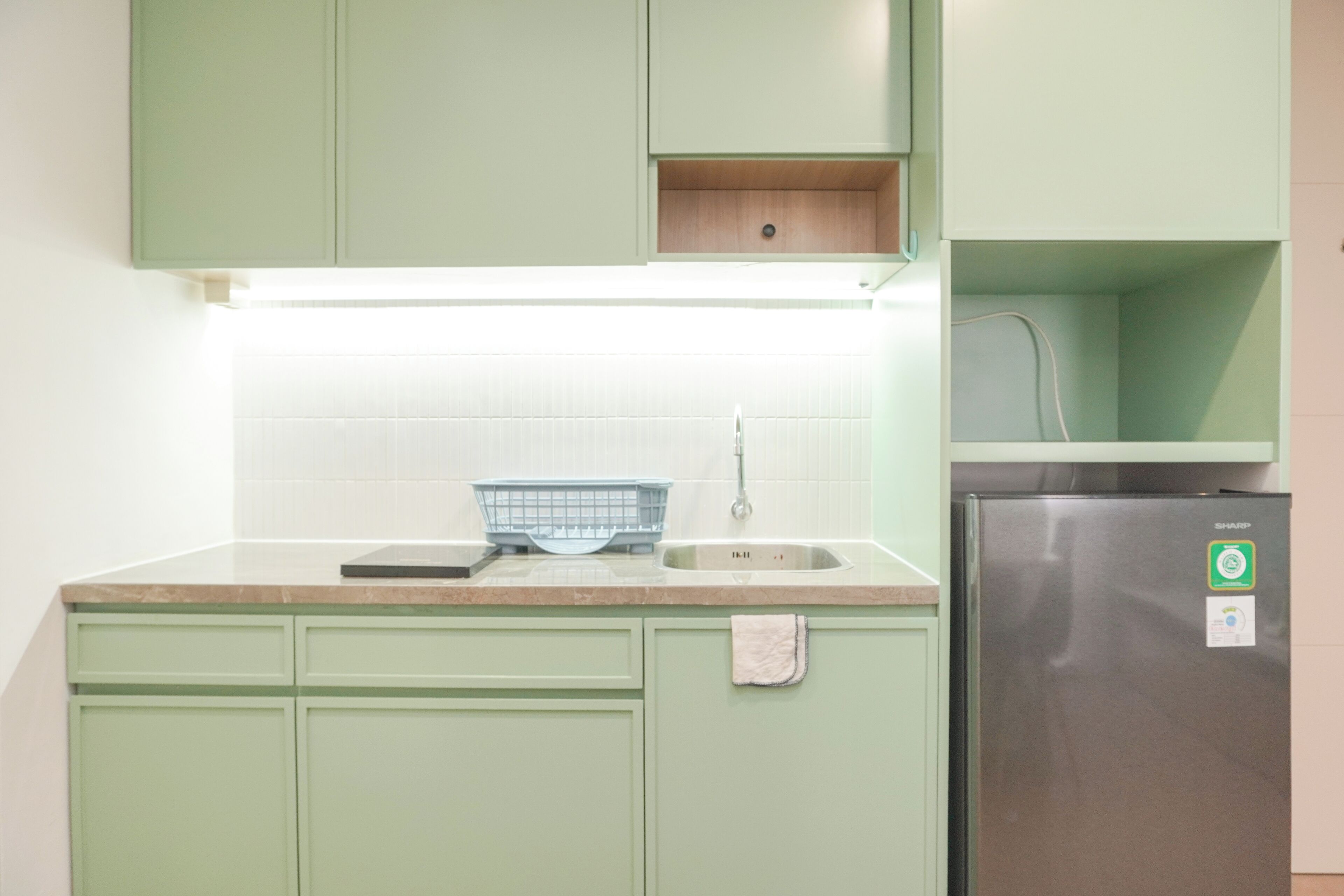 A kitchen with green cabinets, a stainless steel refrigerator, a sink, and a lighted countertop.