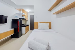 Ett kompakt hotellrum med en säng, en TV, ett kylskåp och ett litet pentry.