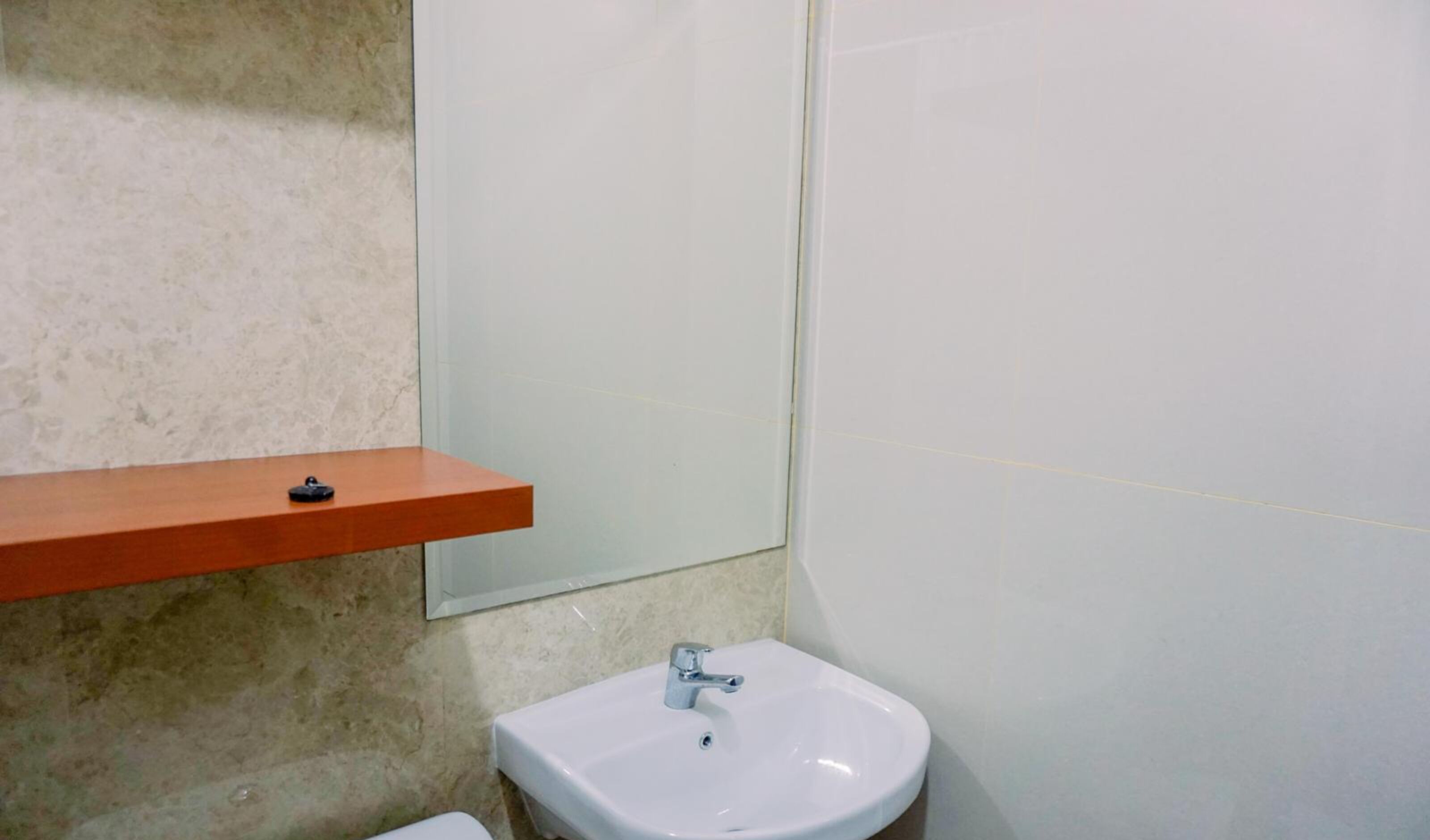 Un baño con un lavabo blanco, un espejo y una repisa de madera.