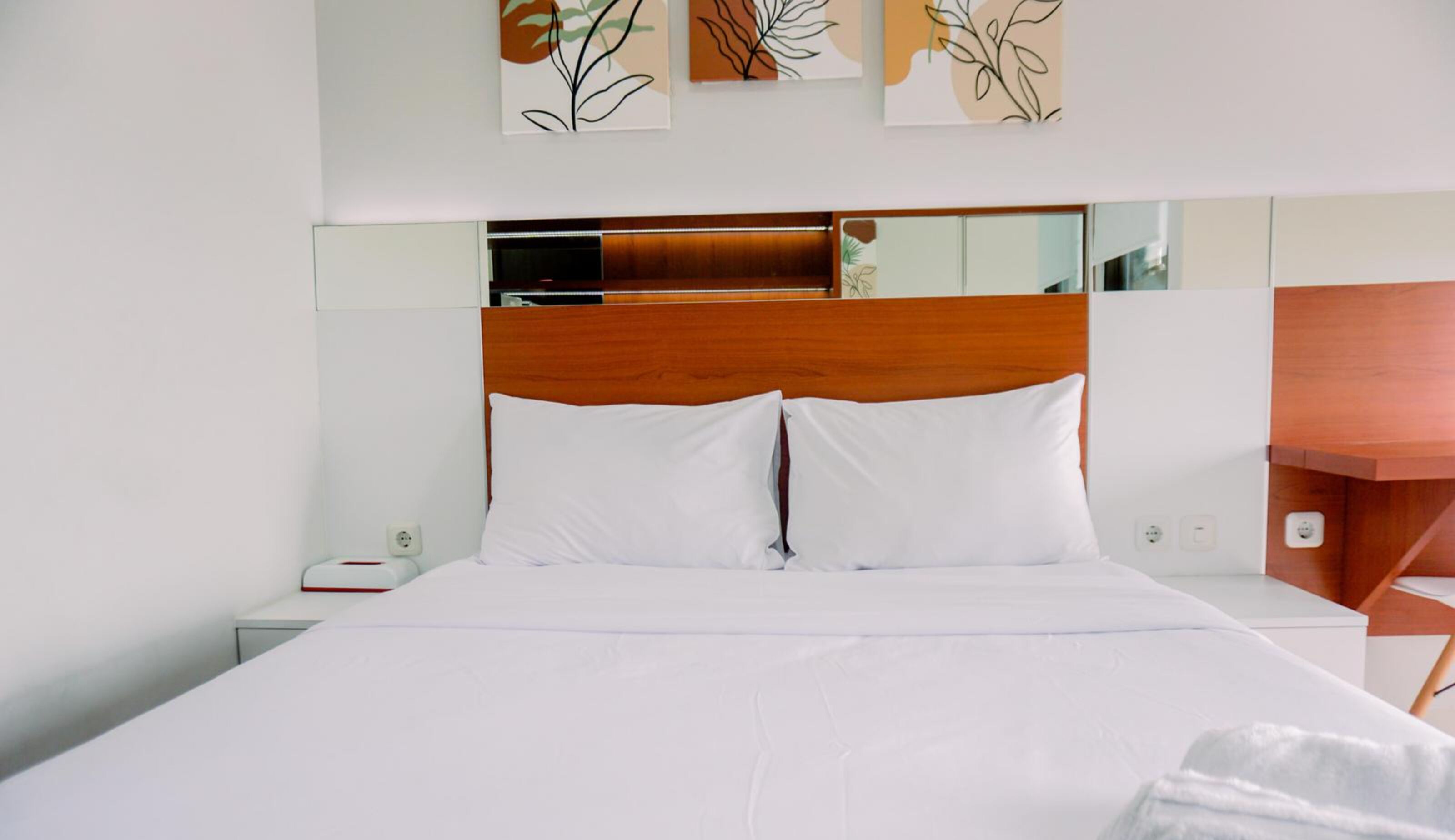 A hotel room with a large bed, white bedding, a wooden headboard, a bedside table, and a wall-mounted TV.