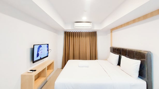 Habitación de hotel con cama, televisor en un pedestal, estante de madera y ventana con cortinas.