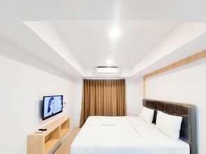 Habitación de hotel con cama, televisor en un pedestal, estante de madera y ventana con cortinas.