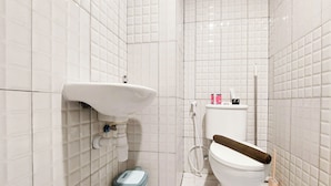 Un baño pequeño y limpio, con azulejos blancos, un lavamanos blanco, un inodoro y un cubo de basura.