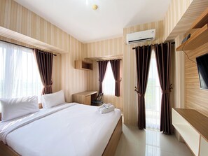 A hotel room with a large bed, a desk, a TV, and an air conditioning unit. - Cozy Stay Studio At Tamansari Mahogany Karawang Apartment (Karawang)