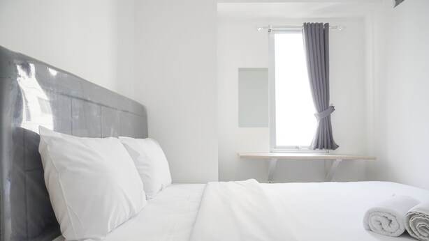 A hotel room with a bed, pillows, a window with curtains, and a bedside table. - Best Deal And Comfort 3Br At Bassura City Apartment (Jakarta)