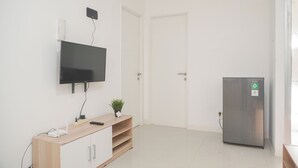 A modern, minimalistic room with a flat-screen TV mounted on the wall, a wooden cabinet with a plant, and a stainless steel refrigerator. - Best Deal And Comfort 3Br At Bassura City Apartment (Jakarta)
