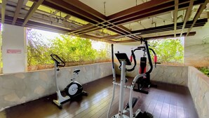 An indoor gym with exercise equipment, stone walls, and a view of greenery outside. - Best Deal And Homey 2Br Bassura City Apartment (Jakarta)
