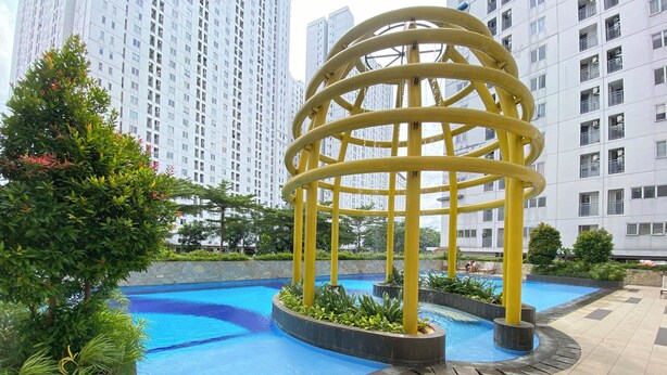A swimming pool with a yellow water feature and surrounding greenery. - Best Deal And Homey 2Br Bassura City Apartment (Jakarta)
