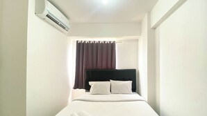 A small, single-bed room with a black headboard, white bedding, and a rolled white towel on the bed. - Best Deal And Homey 2Br Bassura City Apartment (Jakarta)