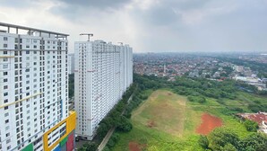 Um edifício alto com vários andares, um jardim no terraço e vista para uma área residencial com casas e vegetação.