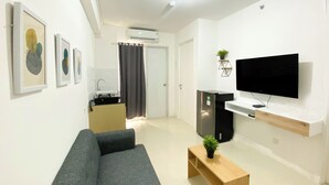 Uma sala de estar moderna com um sofá cinzento, uma mesa de centro de madeira com uma planta, uma televisão de tela plana em uma parede branca e quadros nas paredes.