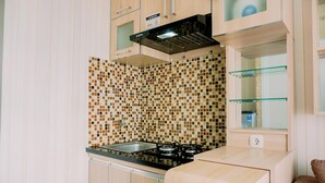 A compact kitchen with a tiled backsplash, a gas stove, and wooden cabinets. - Comfort Stay 2Br At Green Pramuka City Apartment (Jakarta)
