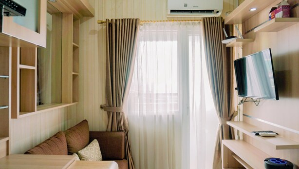 A hotel room with a bed, a TV, a desk, and a window with curtains. - Comfort Stay 2Br At Green Pramuka City Apartment (Jakarta)