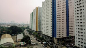 A high-rise building with multiple floors, a parking lot in front, and a cityscape in the background. - Comfort Stay 2Br At Green Pramuka City Apartment (Jakarta)