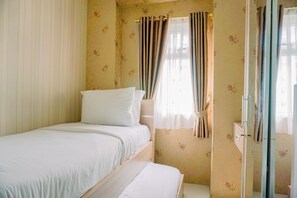 A small, single-bed room with a wooden headboard, a bedside table, and a window with curtains. - Comfort Stay 2Br At Green Pramuka City Apartment (Jakarta)