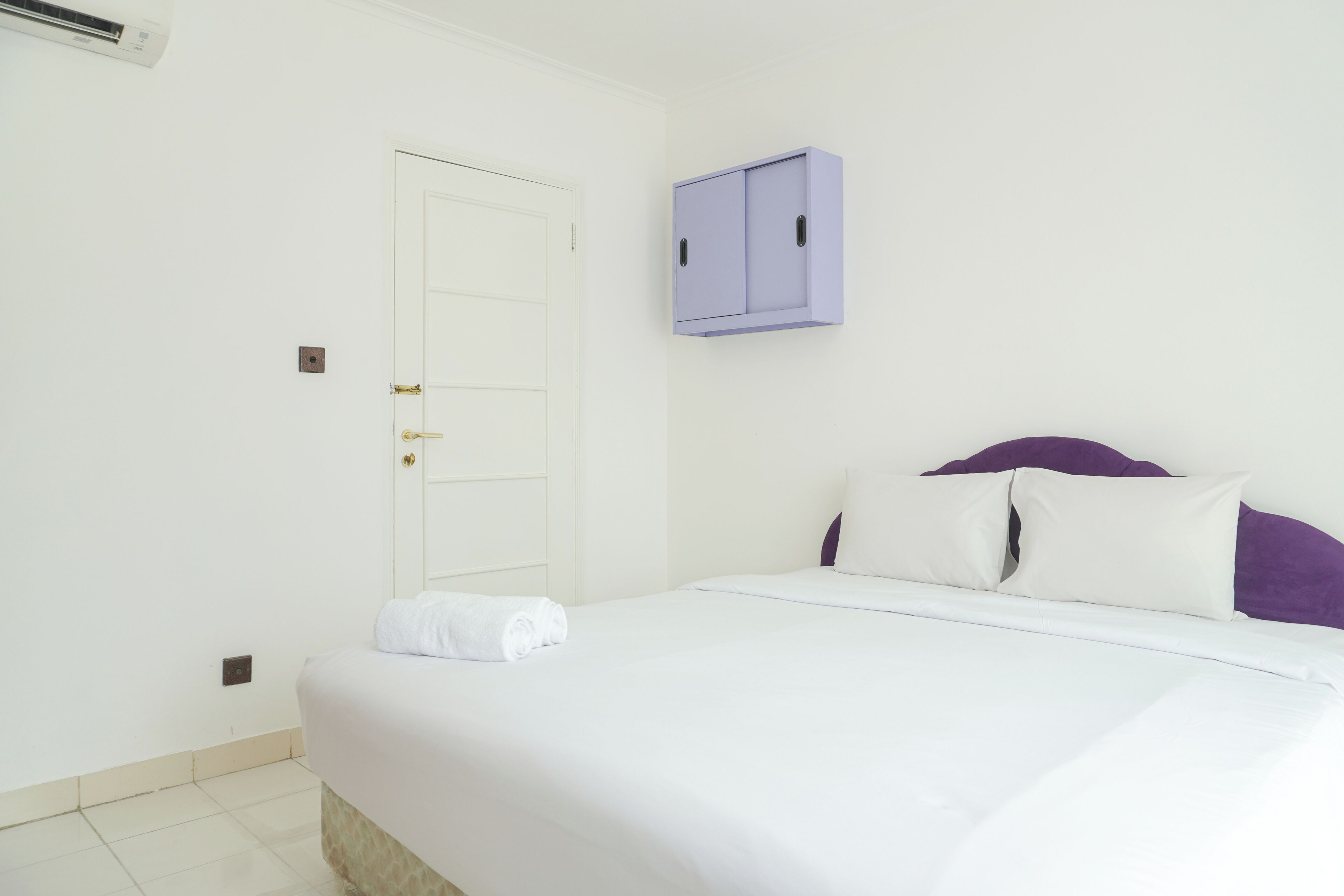 A hotel room with a bed, a white door, and a purple cabinet.