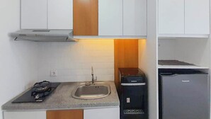 A compact kitchen with white cabinets, a stainless steel sink, a gas stove, and a compact refrigerator.